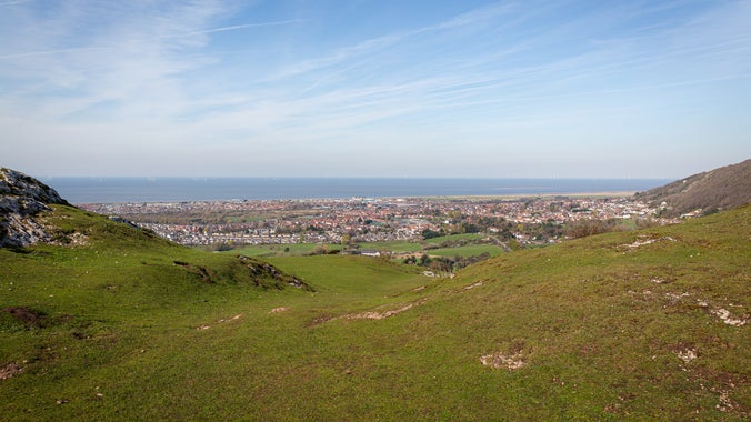 Graig Fawr with rocky, grassy terrain, a village, and the sea in the background.